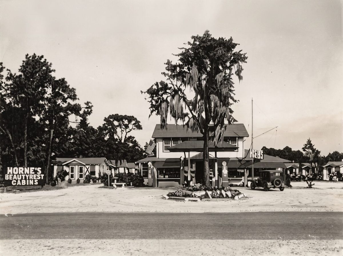 Illustration of the Beauty Rest Cabins motor court soon after it was built in 1921, with crisp white cabins, a young oak, and early 1920s cars